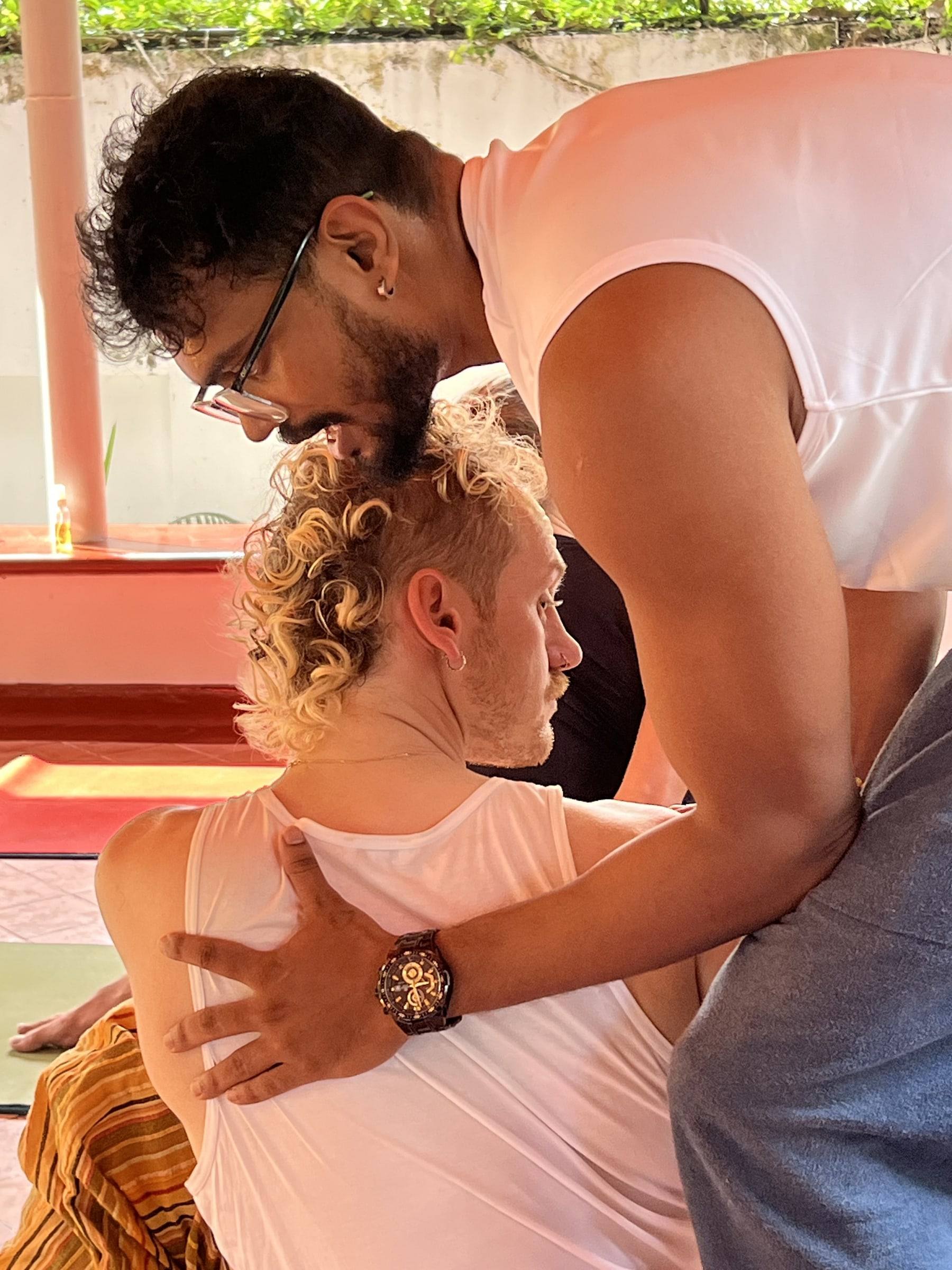 A close, careful hands-on adjustment to a student’s shoulders during a seated posture
