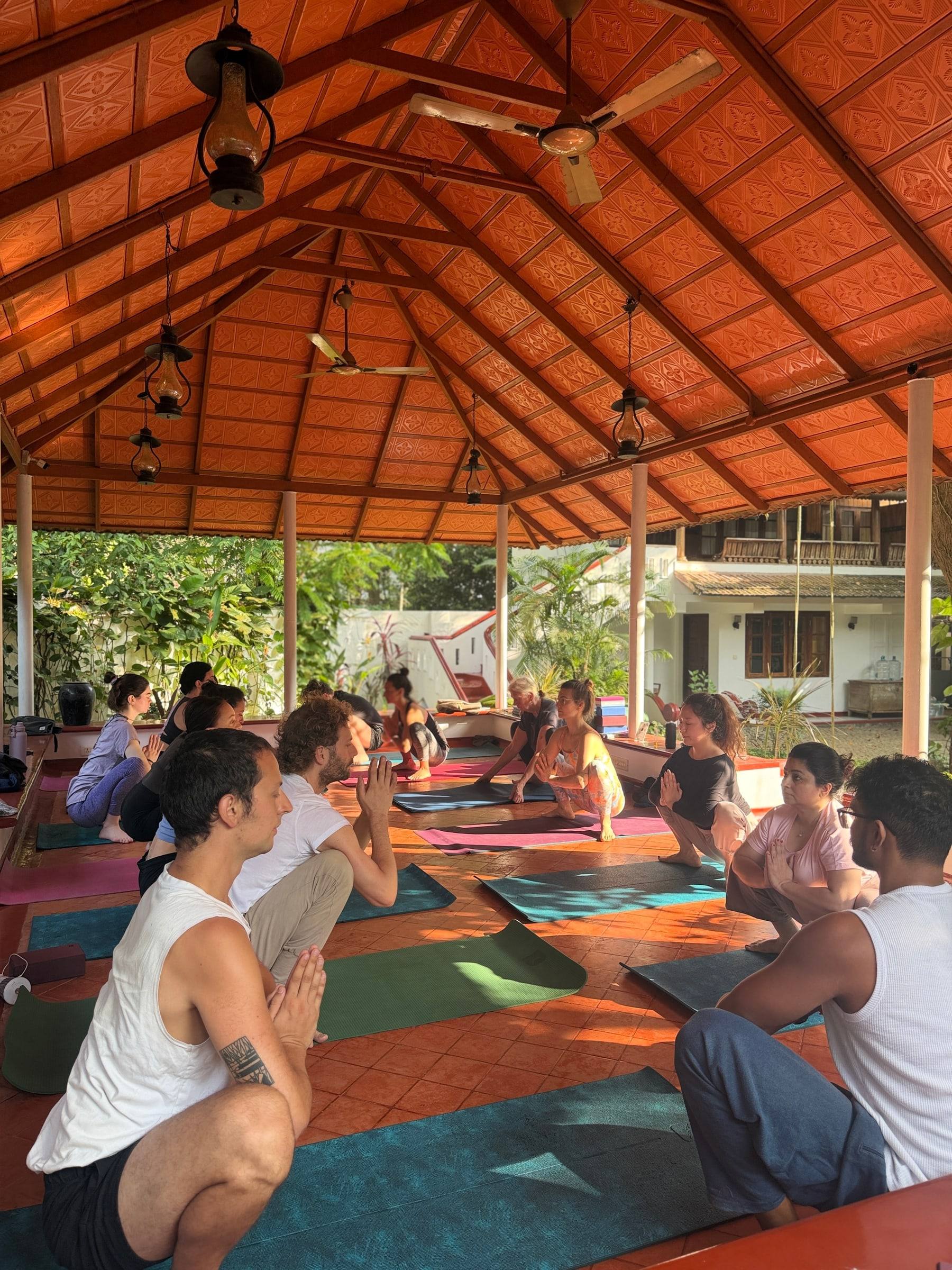 A class squatting with palms joined in the pavilion, lanterns hanging from the tiled roof