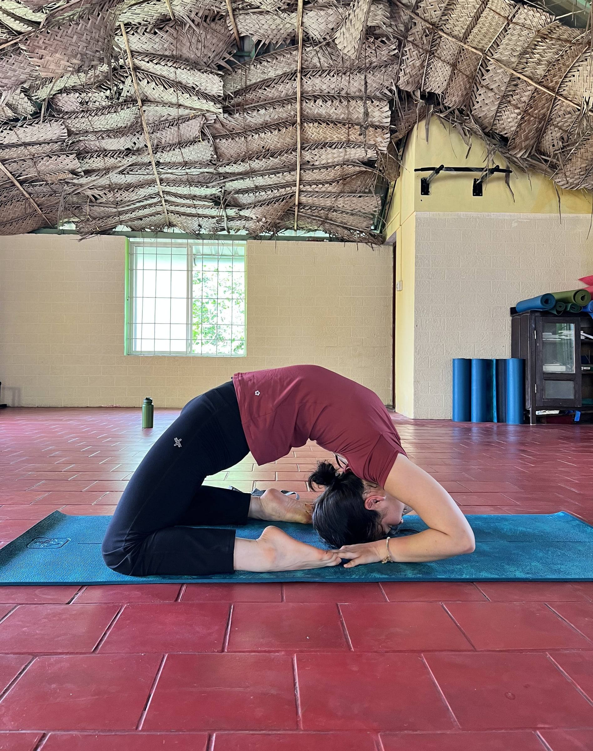 A student in a kneeling backbend on the red floor of the indoor shala