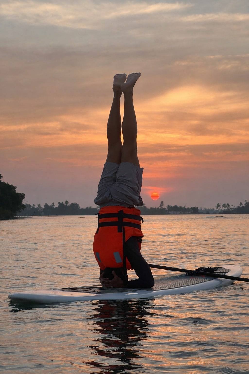 A headstand on a paddleboard on the backwater at sunset, the sun sitting on the horizon